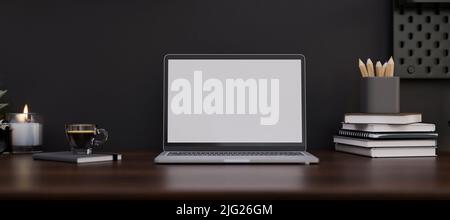 Moderner, dunkler, stilvoller Arbeitsplatz mit Notebook-Laptop-Modell mit weißem Bildschirm, Schreibwaren, Buch und einer Tasse Kaffee auf einem dunklen Holztisch über der schwarzen Wand. 3 Stockfoto