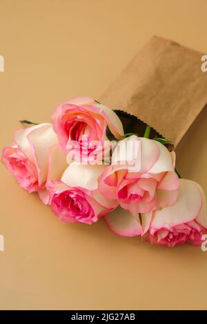 Zarte rosafarbene Rosen in einer Bastelpapiertasche auf beigem Hintergrund. Minimalistisch trendige Komposition. Abstrakte Kunstidee. Romantische rosa Rosenblüten in Pastelltönen. Moderne Ästhetik. Neutrale Erdtöne. Grußkarte Hintergrund Kopierbereich Banner Stockfoto