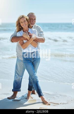 Porträt eines glücklichen und liebevollen reifen Paares, das im Sommer einen Tag am Strand genießt. Fröhlicher, liebevoller älterer Ehemann umarmt seine fröhliche Frau, während er sich umarmt Stockfoto