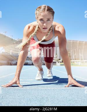 Seriöse weibliche Athletin an der Startlinie bei einem Bahnrennen im Stadion. Fit Sportlerin geistig und körperlich bereit zu starten Stockfoto