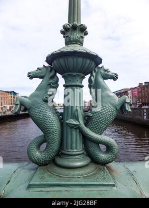 Zwei gusseiserne Seepferde aus dem 19.. Jahrhundert (Hippocampi) schmücken diesen Laternenpfosten auf der Grattan Bridge über den Fluss Liffey in Dublin, Irland. Stockfoto