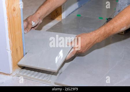 Die Anwendung von Fliesenkleber auf den Boden während des Prozesses der Verlegung von keramischen Fliesen auf eine klebstoffverschmierte Oberfläche Stockfoto