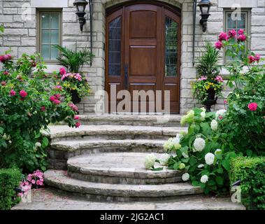 Haupteingang mit eleganter hölzerner Haustür, umgeben von wunderschönen Blumen Stockfoto