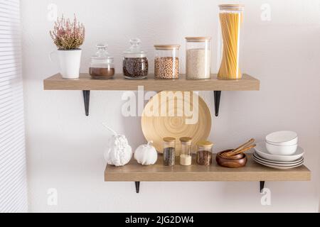 Offene Holzregale mit verschiedenen Gläsern mit einem Holzdeckel gefüllt mit Gewürzen, Kaffee, Spaghetti. Stilvolle Einrichtung in der modernen Küche. Vorderansicht Stockfoto