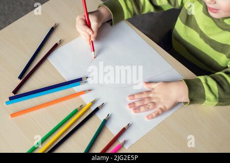 Kleine Kinderzeichnung mit Buntstiften auf weißem Papier, die am Tisch sitzt. Draufsicht. Stockfoto