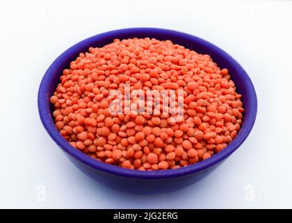 Haufen roter Linsen oder Musur Dal Bohnen in einer blauen Schale isoliert auf unebenem weißen Hintergrund. Selektiver Fokus auf die Mitte. Stockfoto