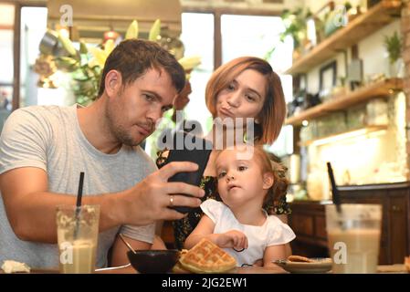 Junge Eltern mit Tochter machen Selfie in einem Café Stockfoto