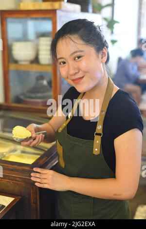 Vietnamesische Kellnerin zeigt eine Kugel hausgemachtes Mango-Eis im Café Stockfoto