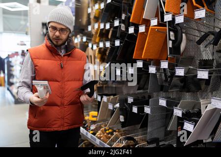 Ein Mann in einem Baumarkt wählt ein Werkzeug für Putzarbeiten Stockfoto