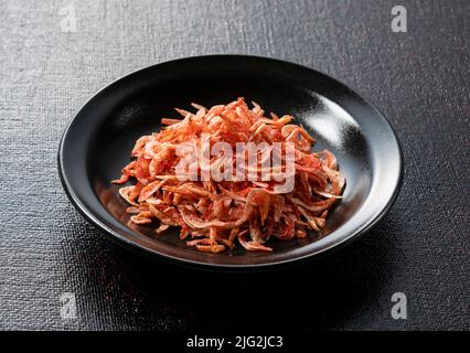 Getrocknete Sakura-Garnelen auf einem Teller auf schwarzem Hintergrund. Das Bild des japanischen Essens. Stockfoto