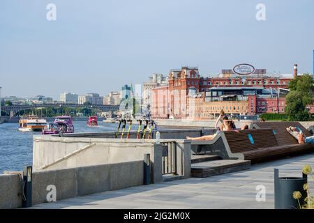 Moskau. Russland. 26. Juni 2021. Die Menschen liegen in Liegestühlen am Ufer des Flusses in der Stadt. An einem sonnigen Sommertag in der Stadt entspannen und sonnen sich die Menschen am Fluss. Stockfoto