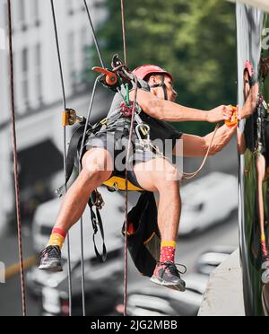 Industrial Bergsteigen professionelle Reiniger in Schutzhelm hängen an Sicherheit Kletterseil und Waschen Gebäudefassade. Mann Reinigung Service Arbeiter wischen Fenster im Freien. Stockfoto