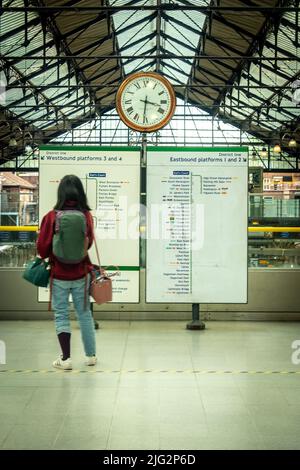 London - 2022. Juni: Passagier schaut auf die Informationafel am Bahnhof Earls Court Stockfoto