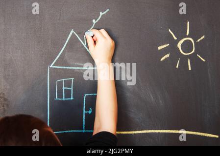 Kind zeichnet auf Tafel Kreidehaus Stockfoto