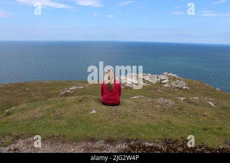 Eine einreisende Frau, die auf der Großen Orme in Llandudno sitzt. Die Frau denkt und denkt nach, gut für ihre körperliche und geistige Gesundheit. Stockfoto