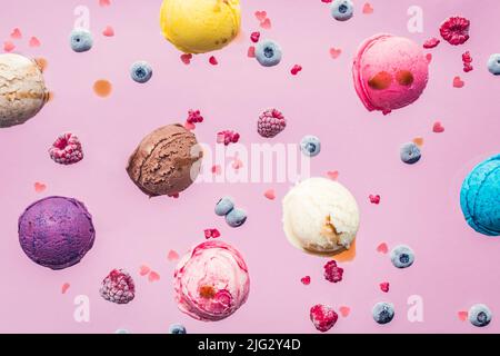 Fallende Eisschaufeln und Beeren auf rosa Hintergrund. Levitation von Lebensmitteln. Buntes Eis Kunst Foto. Stockfoto