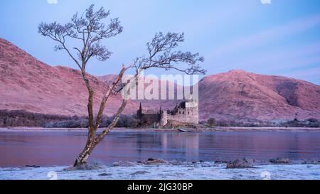 Sonnenaufgang an einem frostigen Wintermorgen mit Spiegelungen des Kilchurn Castle in Loch Awe, Highlands, Schottland Stockfoto