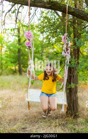 Nettes lächelndes Mädchen, das Spaß auf einer Schaukel im Baumwald hat Stockfoto