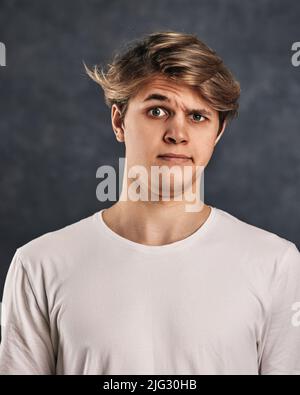 Junger, hübscher Mann mit einem Zweifel im Gesicht im T-Shirt Stockfoto