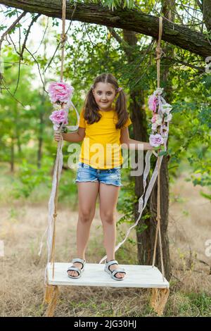 Nettes lächelndes Mädchen, das Spaß auf einer Schaukel im Baumwald hat Stockfoto