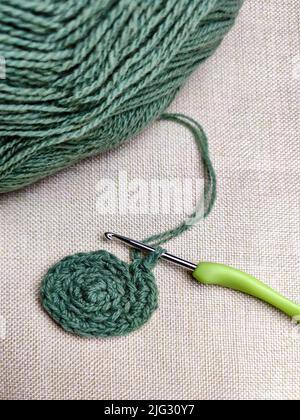Grüner Garnfaden mit einem Haken zum Stricken auf grauem Hintergrund aus Stoff, Hobbies. Speicherplatz kopieren. Selektiver Fokus. Stockfoto