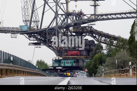 Profen, Deutschland. 07.. Juli 2022. Eine große Tagebau-Maschine fährt auf einer Straße. Der Streuer, der rund 3.800 Tonnen wiegt, wird zum Transport von Überlast im Braunkohlenbergbau verwendet. Die 60 Meter hohe Struktur bewegt sich mit einer Geschwindigkeit von sechs Metern pro Minute. Der Grund für die Verlegung ist eine geplante Generalreparatur. Kredit: Sebastian Willnow/dpa/Alamy Live Nachrichten Stockfoto