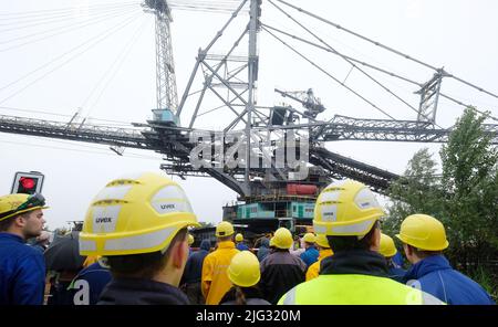 Profen, Deutschland. 07.. Juli 2022. Eine große Tagebaumaschine fährt vor Zuschauern entlang einer Straße. Der 3.800-Tonnen-Streuer wird zum Transport der Überlast im Braunkohlebergbau eingesetzt. Die 60 Meter hohe Struktur bewegt sich mit einer Geschwindigkeit von sechs Metern pro Minute. Der Grund für die Verlegung ist eine geplante Generalreparatur. Kredit: Sebastian Willnow/dpa/Alamy Live Nachrichten Stockfoto