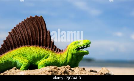 Grüner Plastikdinosaurier am Strand mit blauem Himmel und Kopierraum Stockfoto