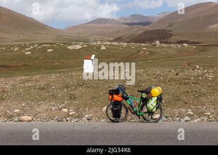 Tourenrad mit Packtaschen steht am Straßenrand vor der Kulisse der Berge. Reisefahrrad. Kirgisistan Stockfoto