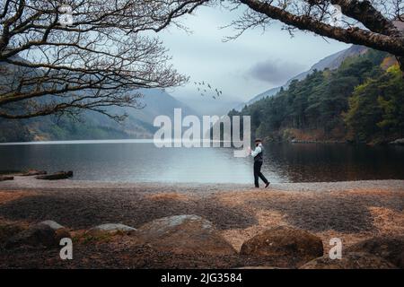Stilvoller Mann, der sein Hemd neben einem See in den Wicklow Mountains, Irland, befestigt. Thema 1920s. Modischer, brutaler, selbstbewusster bärtiger Mann. Stockfoto