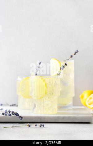 Glitzernde Sommerlemonade aus Lavendel in Gläsern auf grauem Hintergrund. Vertikales Format. Nahaufnahme. Sommergetränke für Party. Stockfoto