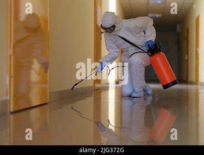 Die Person in Schutzkleidung desinfiziert Büros und Korridore, um eine Ausbreitung von COVID-19 zu verhindern Stockfoto