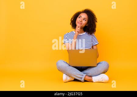 Ganzkörper-Porträt von gesinnten ziemlich Dame Arm berühren Kinn aussehen leeren Raum halten Netbook isoliert auf gelbem Hintergrund Stockfoto