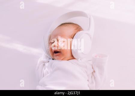 Das Kind trägt Kopfhörer. Frohes Baby. Ein neugeborenes Baby. Weiß auf Weiß Stockfoto