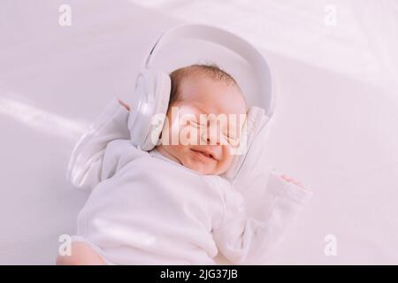 Das Kind trägt Kopfhörer. Frohes Baby. Ein neugeborenes Baby. Weiß auf Weiß Stockfoto