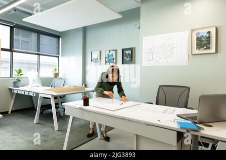 Asiatische junge Architektin zeichnet Blaupause am Tisch im Büro Stockfoto