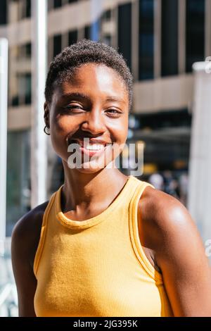Porträt einer fröhlichen afrikanischen jungen Frau, die an einem sonnigen Tag die Kamera anschaut. Sie trägt ein sommerliches gelbes T-Shirt Stockfoto