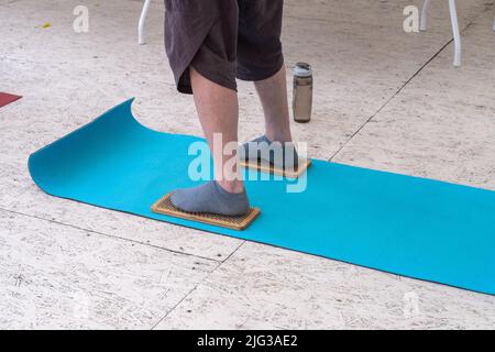 Herrenfüße in Socken stehen auf einem Brett mit scharfen Nägeln. Ein Mann, der auf einer Yogamatte und auf Brettern mit Nägeln steht, bereitet sich auf die Yoga-Praxis vor. Sadhu Yog Stockfoto