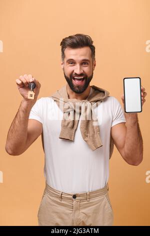 Porträt eines fröhlichen Mannes, der einen Autoschlüssel hält, präsentiert Smartphone isoliert auf braunem Hintergrund im Studio mit Kopierraum Stockfoto