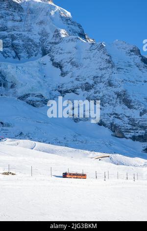 Kleine Scheidegg, Schweiz - 10 01 2021: Ein roter Zug fährt Richtung Jungfraujoch, dem Gipfel Europas. Oben sind die Schneeberge. Stockfoto