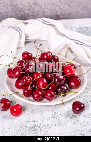 Frische Kirsche. Reife Kirschen auf einem Teller auf einem steinernen Hintergrund. Bulk Kirschen. Nahaufnahme Stockfoto