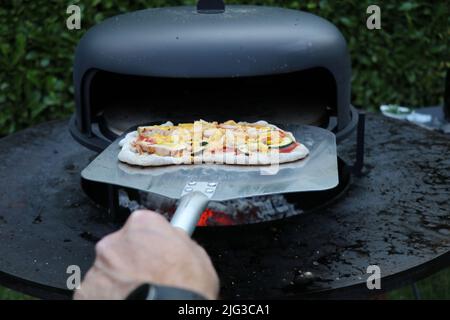 Eine hausgemachte, rustikale Pizza, die aus einem Holzofen im Freien genommen wird Stockfoto