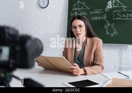 Der Lehrer hält das Notebook in der Nähe des digitalen Tablets und der Kamera im Klassenzimmer Stockfoto