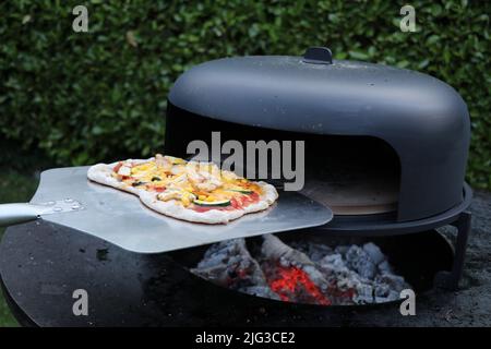 Eine hausgemachte, rustikale Pizza, die aus einem Holzofen im Freien genommen wird Stockfoto