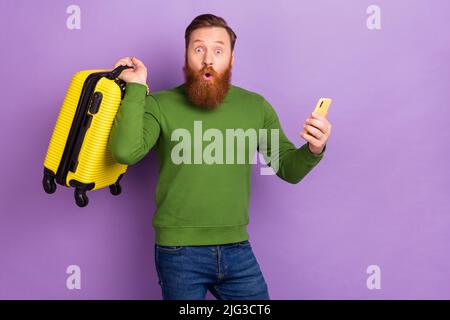 Portrait von schönen trendy stauned Kerl mit Gerät kaufen Tour Tickets Buch isoliert über helle violette lila Farbe Hintergrund Stockfoto