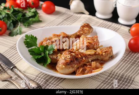 Gebackene Hähnchendrumsticks mit Gemüse, Gewürzen und Petersilie auf weißem Teller, Close-Up Stockfoto