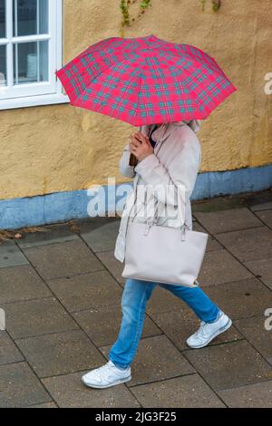 Besucher, die bei strömendem Regen in Oxford, Oxfordshire, Großbritannien, an einem regnerischen Tag im August mit einem Tartanschirm spazieren gehen Stockfoto