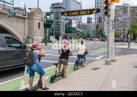 Boston, MA, USA, 11. Juni 2022: Menschen auf Fahrrädern und Motorrollern in der Fahrradspur warten auf die Verkehrsampel in der geschäftigen Innenstadt. Stockfoto