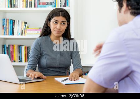 Skeptischer südamerikanischer Business Trainee im Gespräch mit einem Kollegen im Büro Stockfoto
