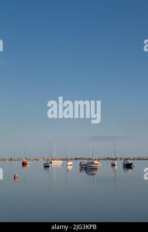 Blick über den Christchurch Harbour in Richtung Mudeford Spit und Mudeford Beachhuts mit Boats on A Clam Day, Christchurch UK Stockfoto